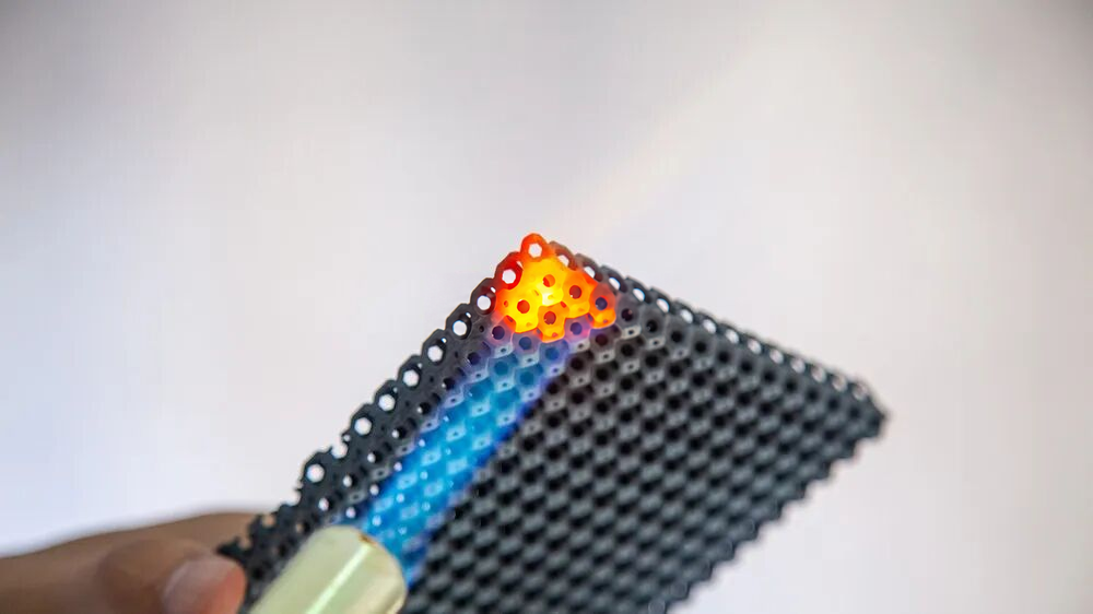 Source photograph: a flame directed at the perforated plate, with a locally glowing region.
